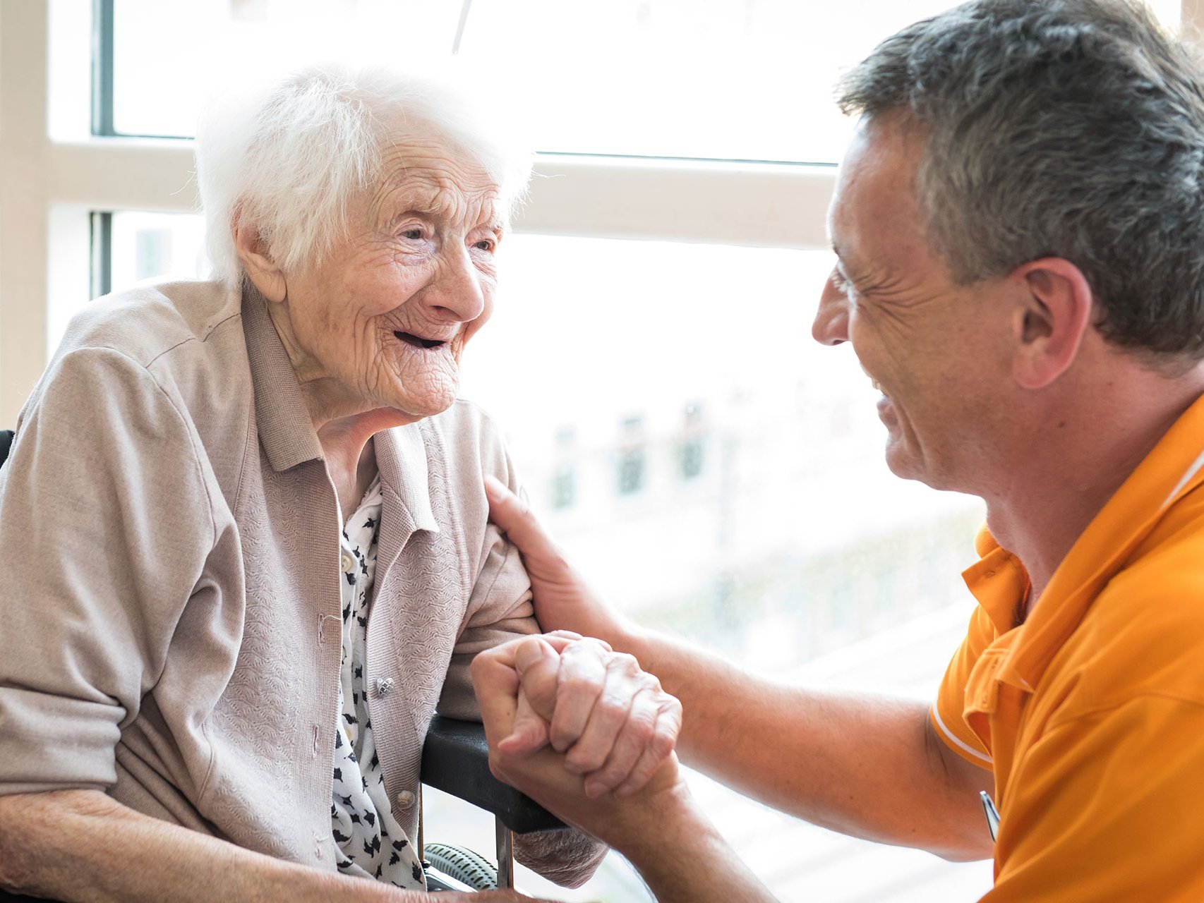 Ein Pfleger hält die Hand einer Bewohnerin - beide lachen