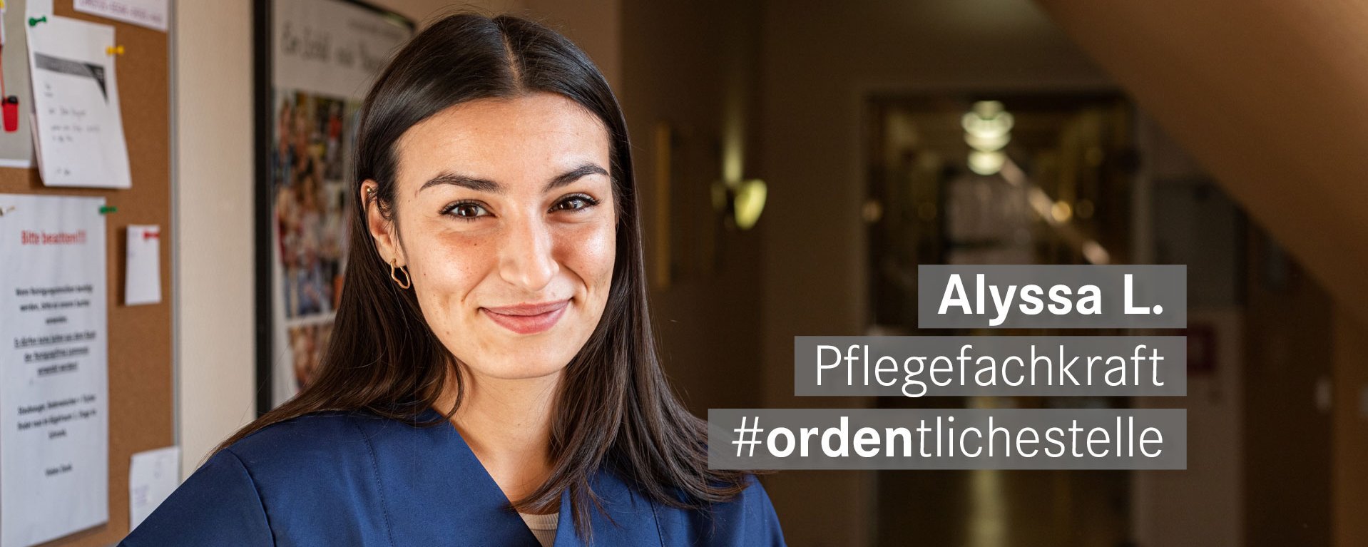 Pflegekraft mit braunen Haaren und Augen laechelt freundlich in die Kamera