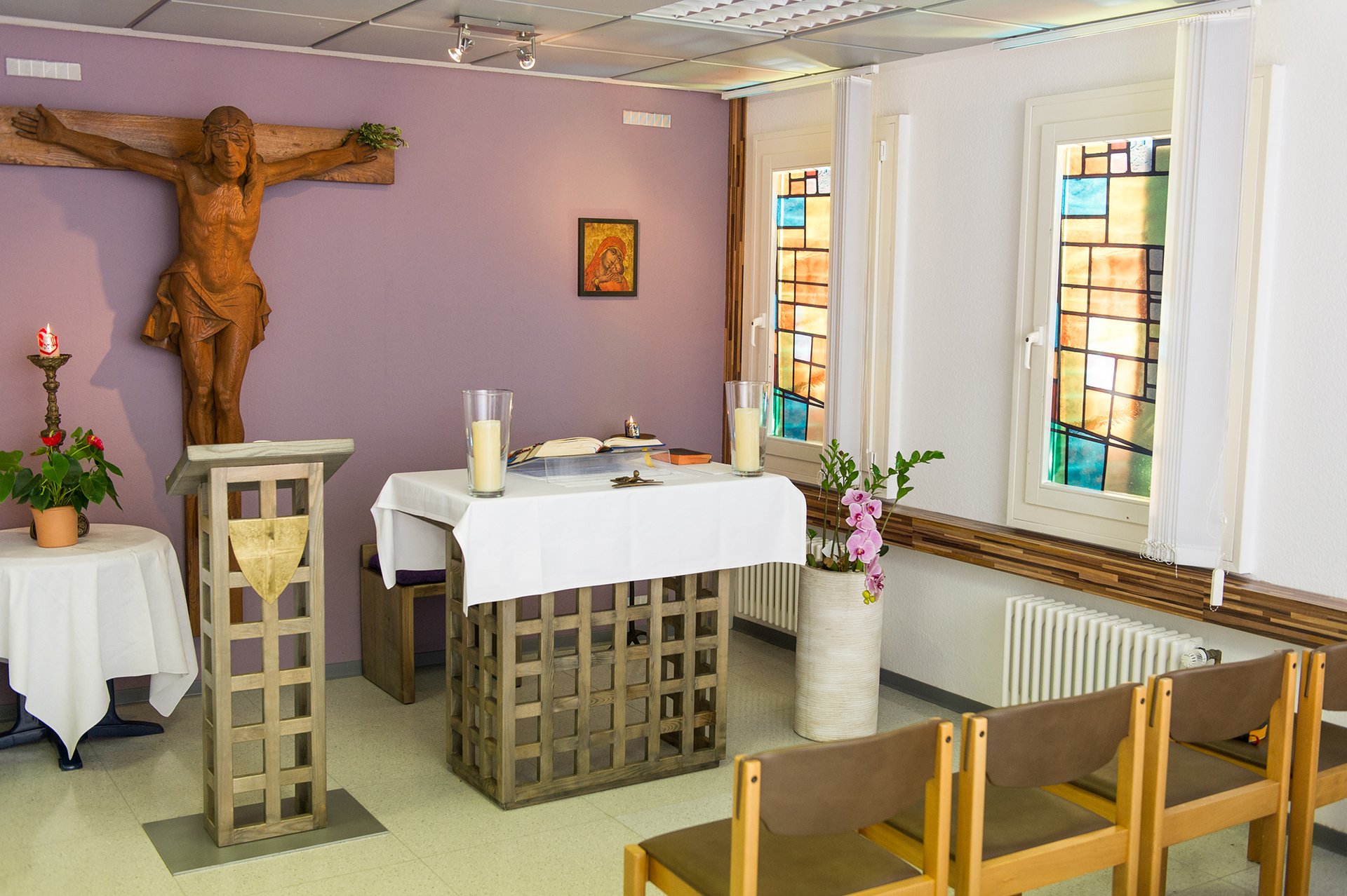 Innanansicht: moderne kleine Kapelle mit Holzkreuz, Osterkerze, kleinem Altar und einer Stuhlreihe